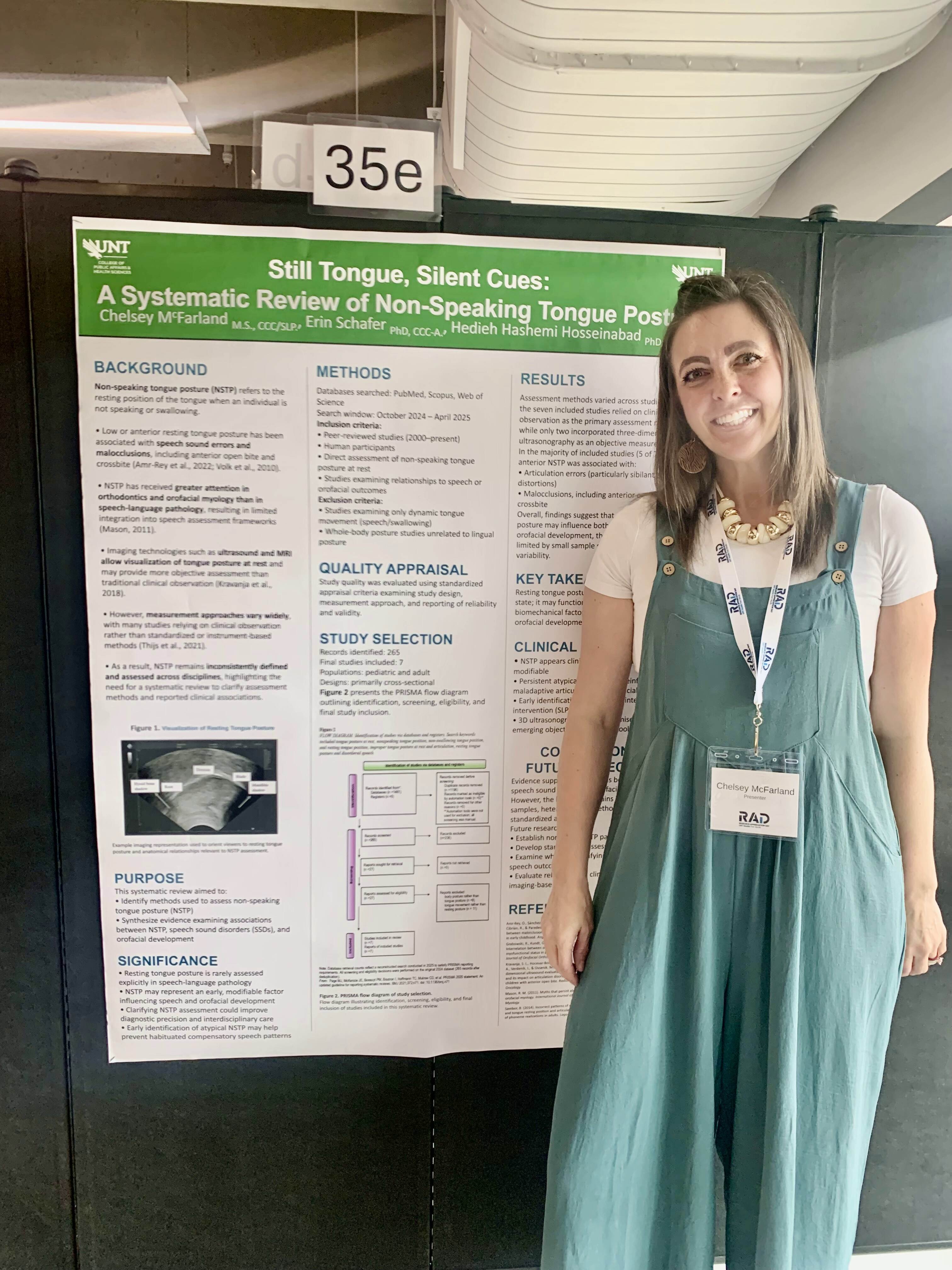 Student in a dress standing to the right of a research presentation poster