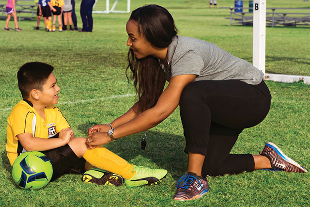 Woman tying boy's shoe on soccer field