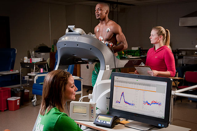 Man running on a treadmill while women work with him