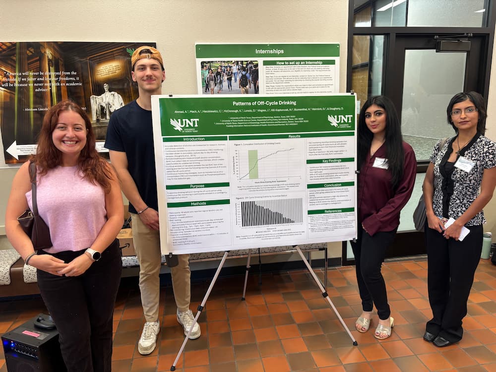 four researchers standing next to research poster